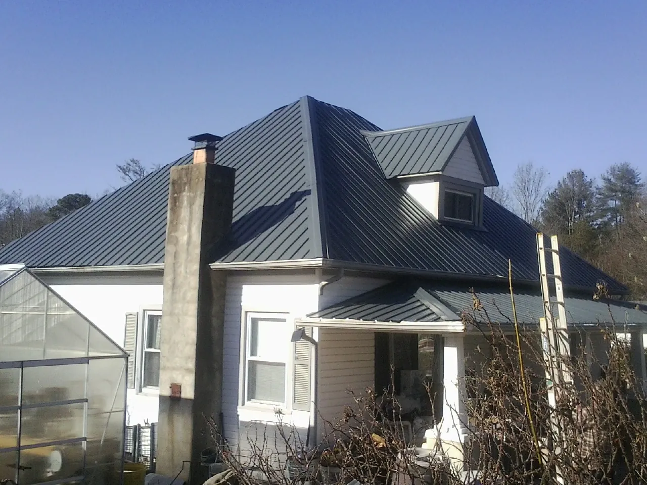 Dark blue standing seam metal roof on a white farmhouse with dormer — Slate & Tile Roof Repair by Roofing Brothers in Blue Bell