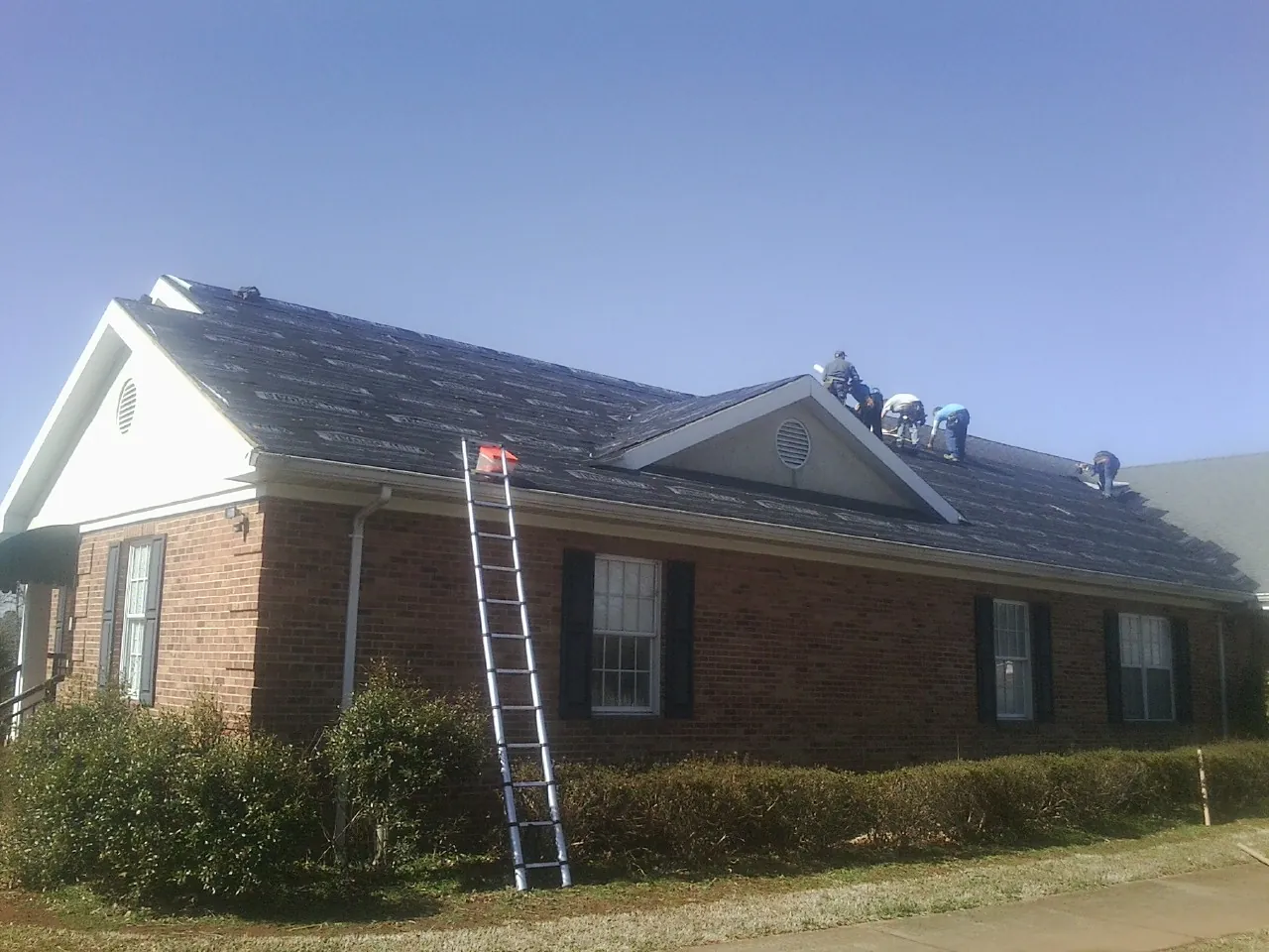 Crew tearing shingles off a brick ranch roof with a ladder set — Emergency Roof Repair work by our crew in Blue Bell