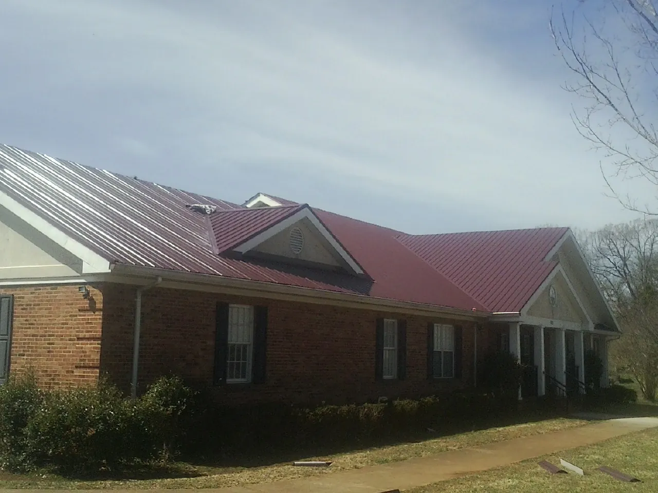 Red metal roof with gabled entries on a long brick building, from a Hail Damage Roof Repair job in Blue Bell