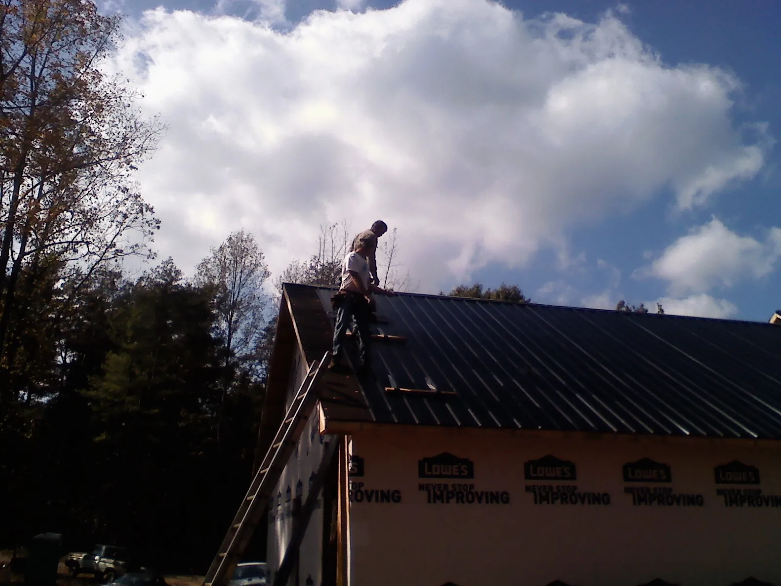 Roofer fastening dark metal panels high against a cloudy sky, from a Roof Inspection job in Blue Bell