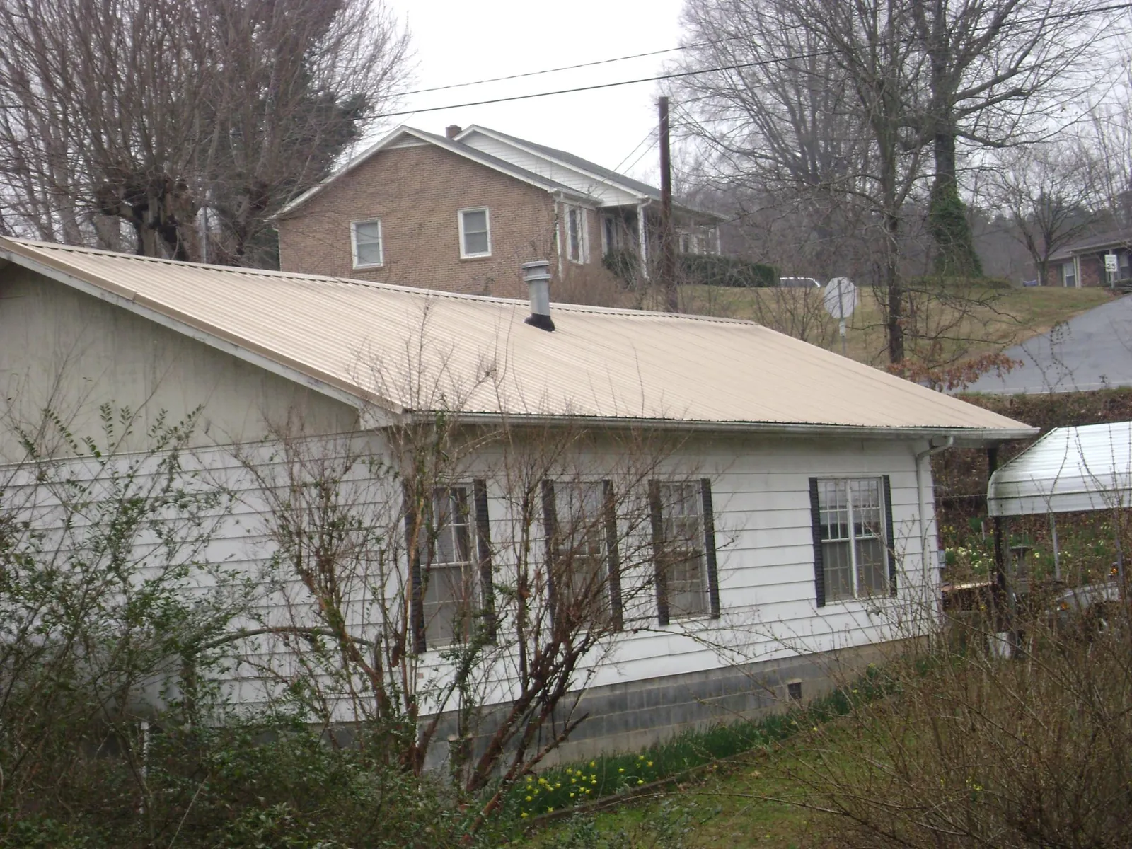Tan metal roof on a white sided house set into a hillside — Commercial Roofing by Roofing Brothers in Blue Bell